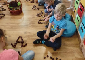 Dzieci układają kształt wielkiej i małej litery A z kasztanów.